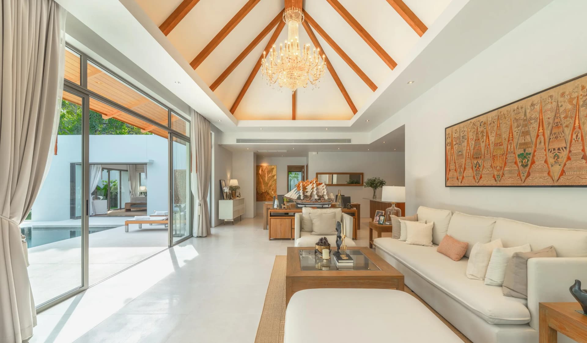Le séjour voûté d’une villa Anchan construite : chevrons en bois, lustre en cristal et baie vitrée coulissante vers la piscine